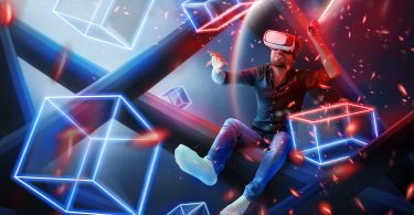 Man with red light saber sitting in blue white and red colored backdrop of geometric boxes type metaverse with headset on