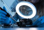 Woman scientist with LED light and soldering iron working on a motherboard