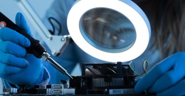 Woman scientist with LED light and soldering iron working on a motherboard