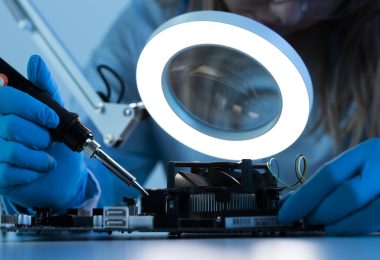 Woman scientist with LED light and soldering iron working on a motherboard