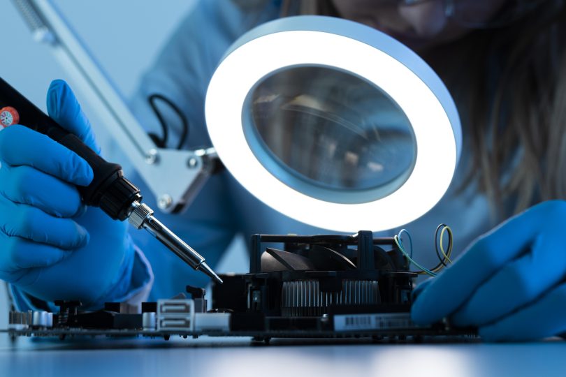 Woman scientist with LED light and soldering iron working on a motherboard