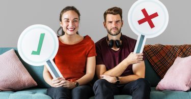 Cheerful couple holding vote icon sitting on a couch